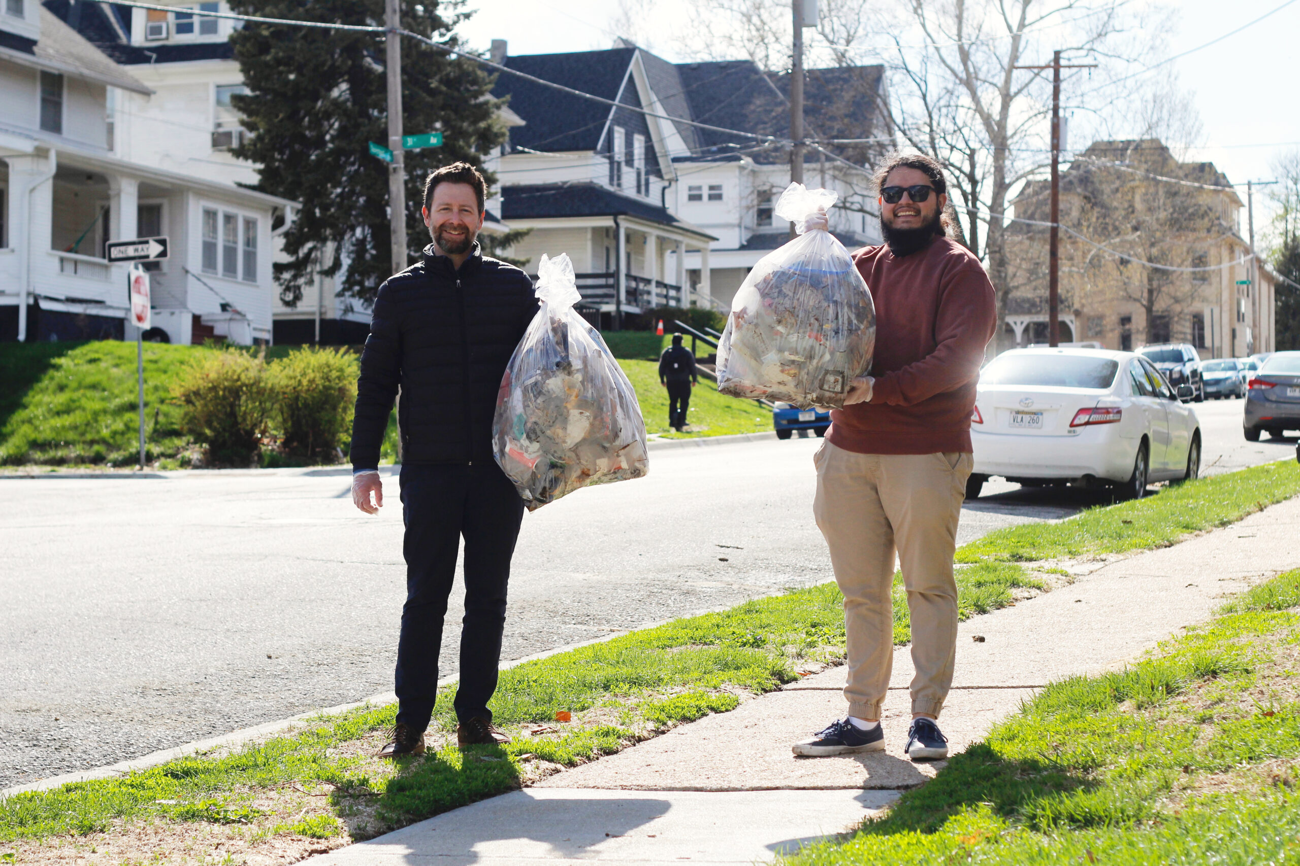Emspace + Lovgren team members Casey and Randy smile while holding large, full trash bags on a Gifford Park neighborhood sidewalk