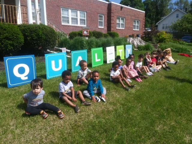 Group of day care kids poses with This Is Quality campaign yard signs