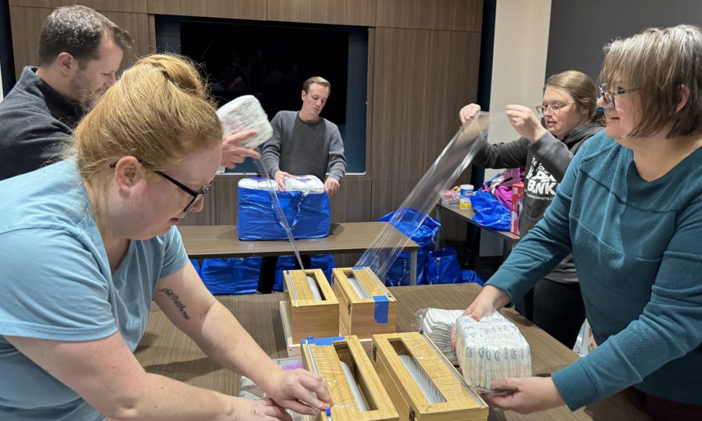 Four Emspace team members and a Nebraska Diaper Bank representative sort and wrap bundles of diapers in an Emspace conference room